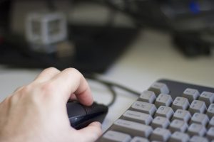 a hand using a computer mouse next to corner of keyboard